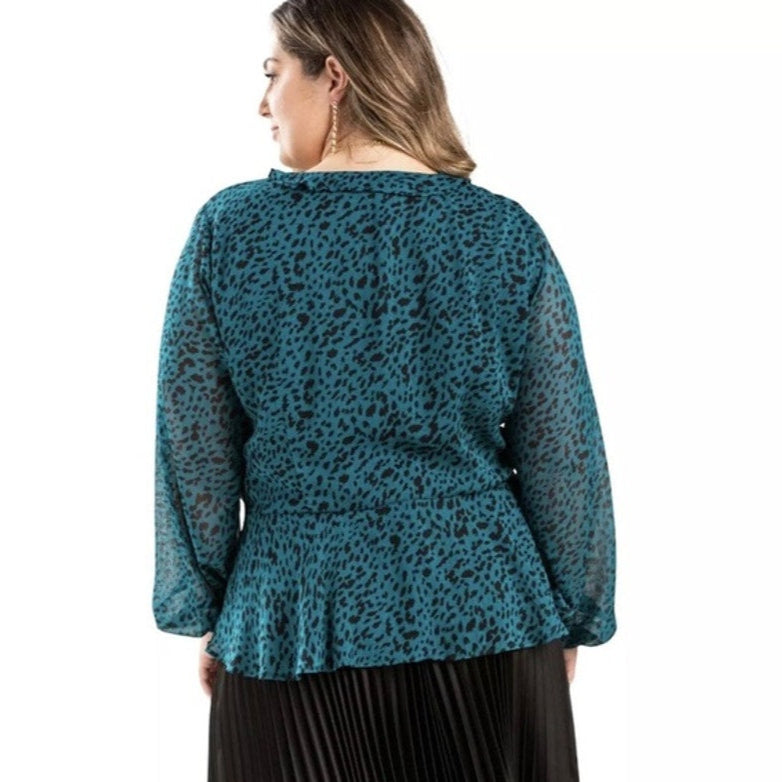 Woman wearing a teal leopard print top with a plain white background