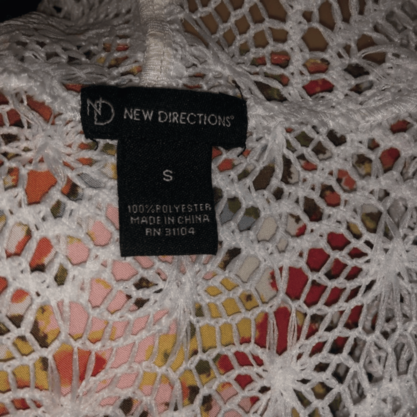 Close-up of a 'New Directions' label on a colorful lace garment.