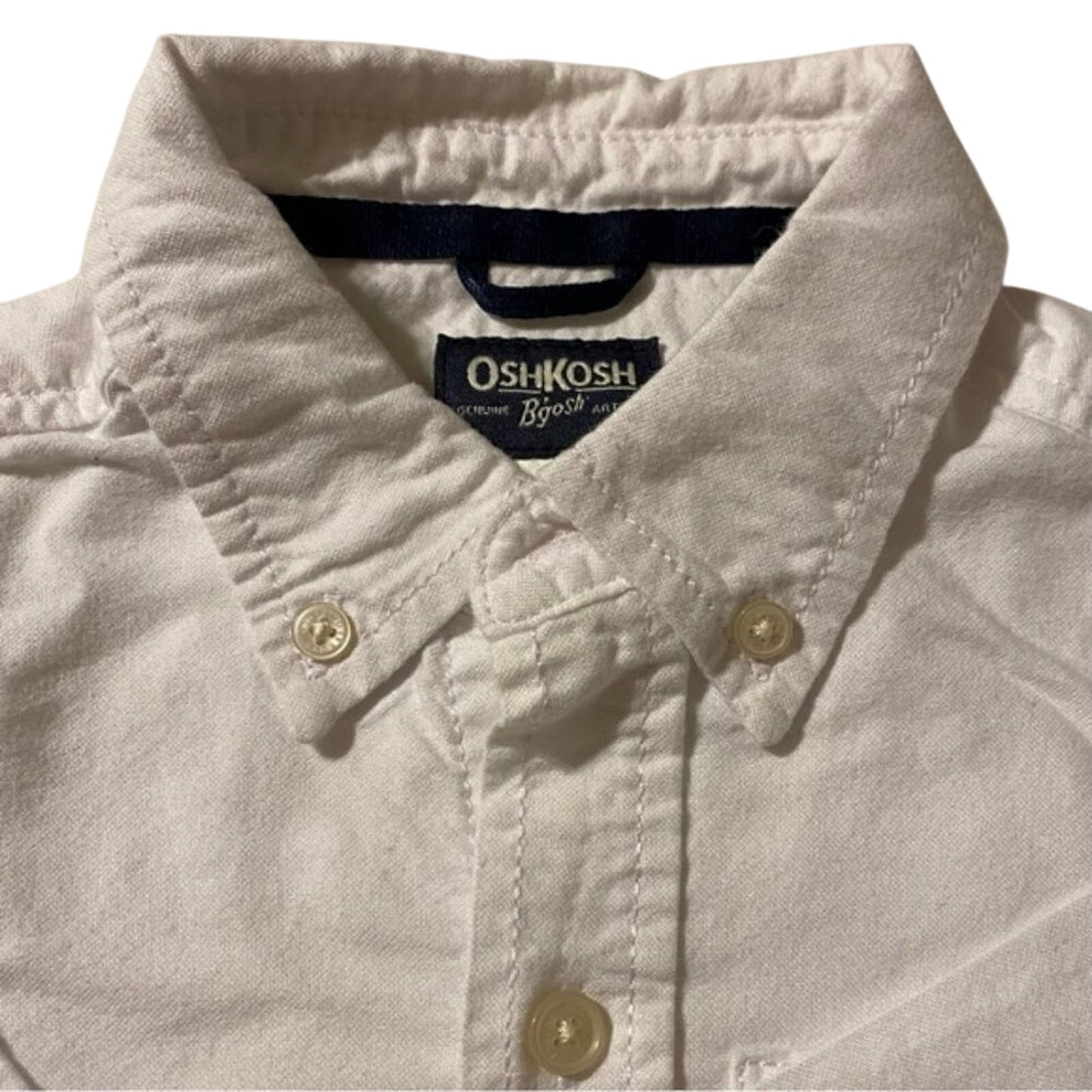Close-up of a light-colored shirt with OshKosh logo on a white background