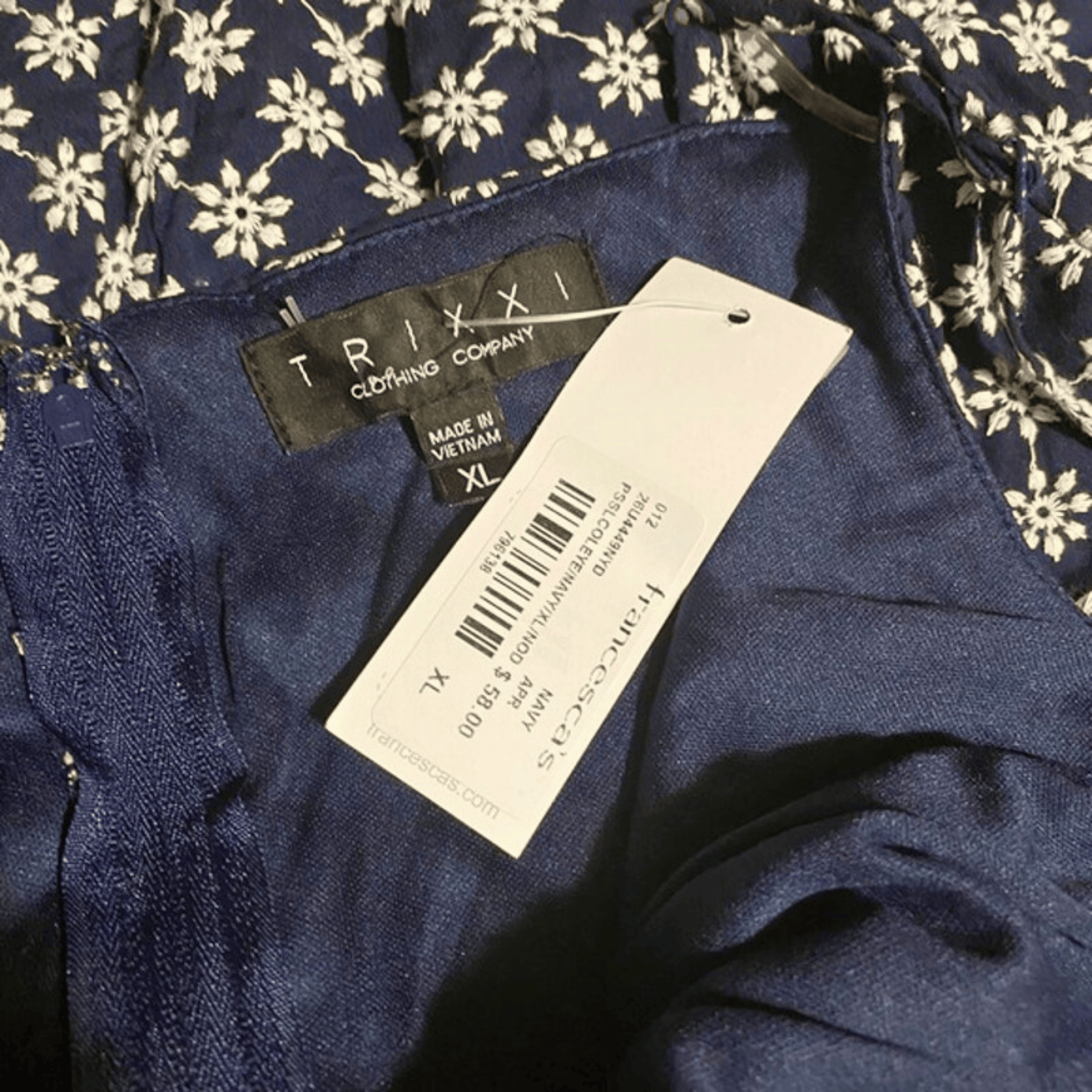 Navy blue garment with TRIXI label and tag on a floral background