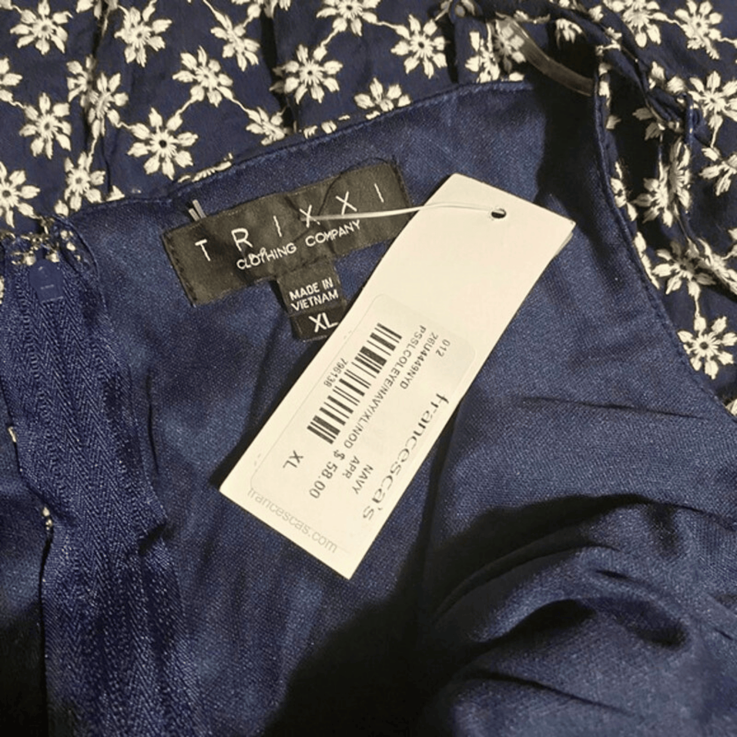 Navy blue garment with TRIXI label and tag on a floral background