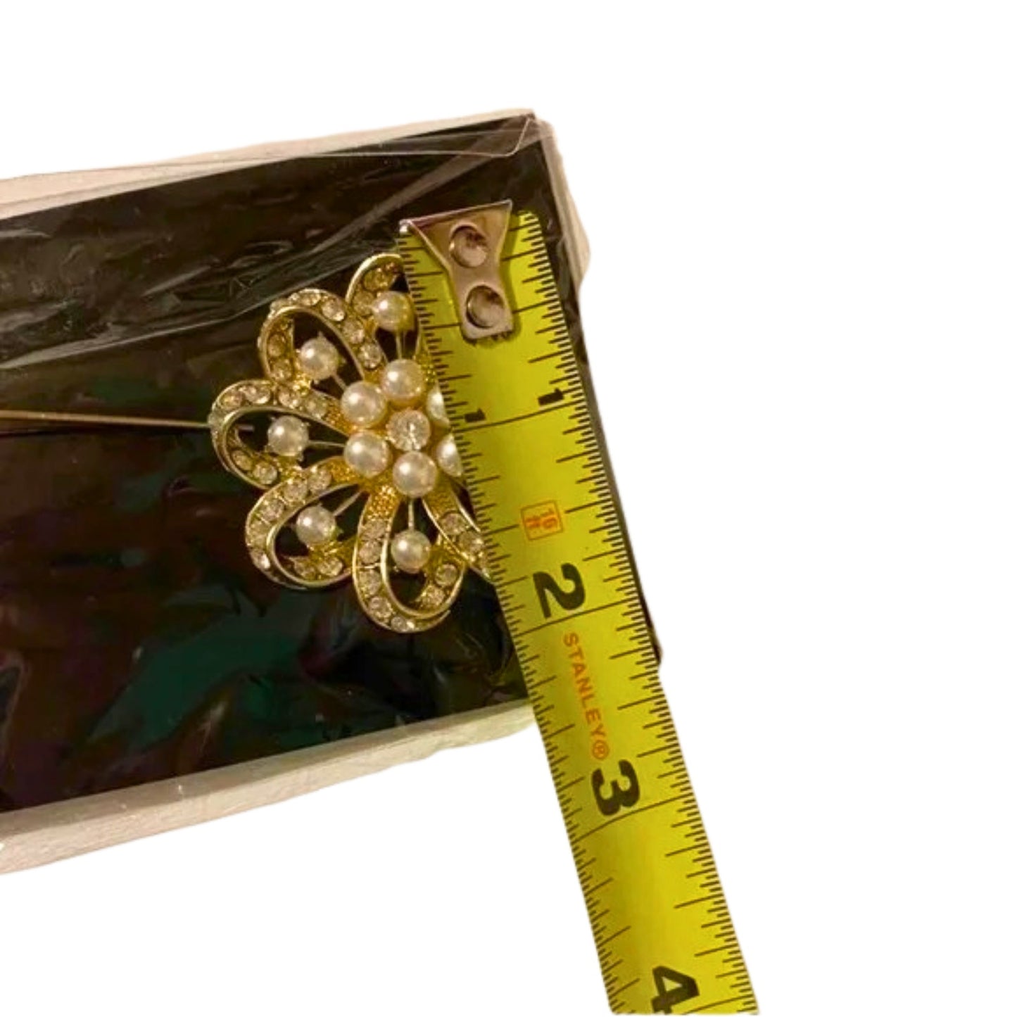 Gold brooch with pearls on a box next to a measuring tape