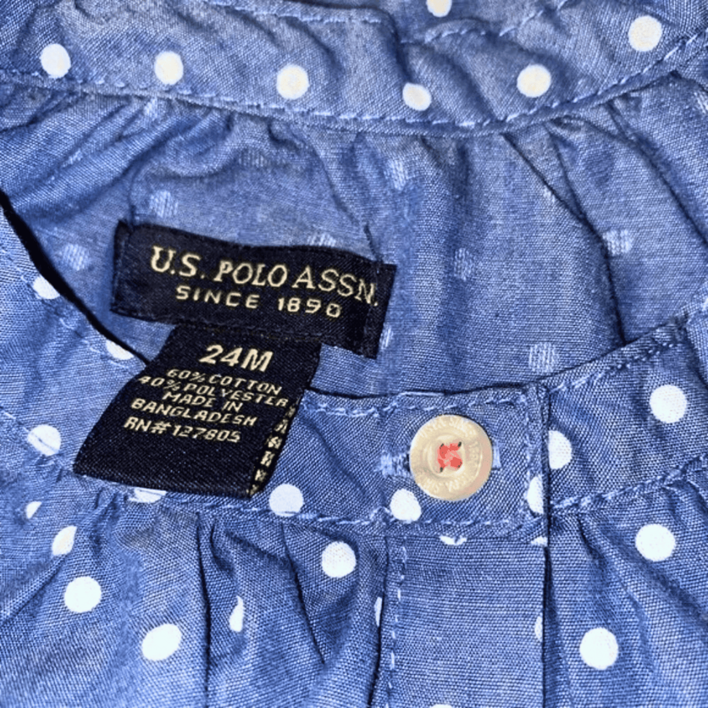 Close-up of U.S. Polo Assn. label on a blue polka dot shirt with a button.