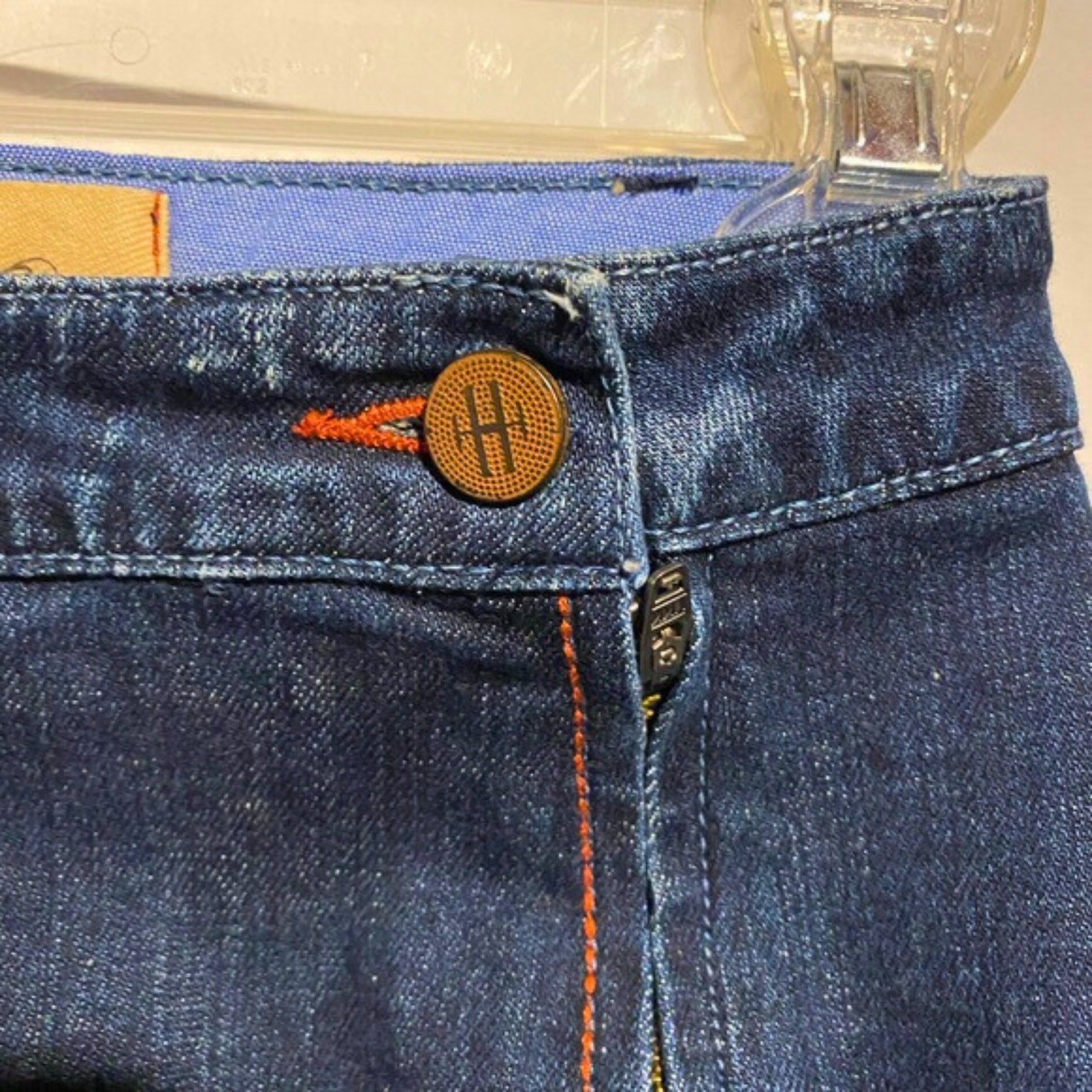 Close-up of blue jeans with a button and zipper, brand logo visible.