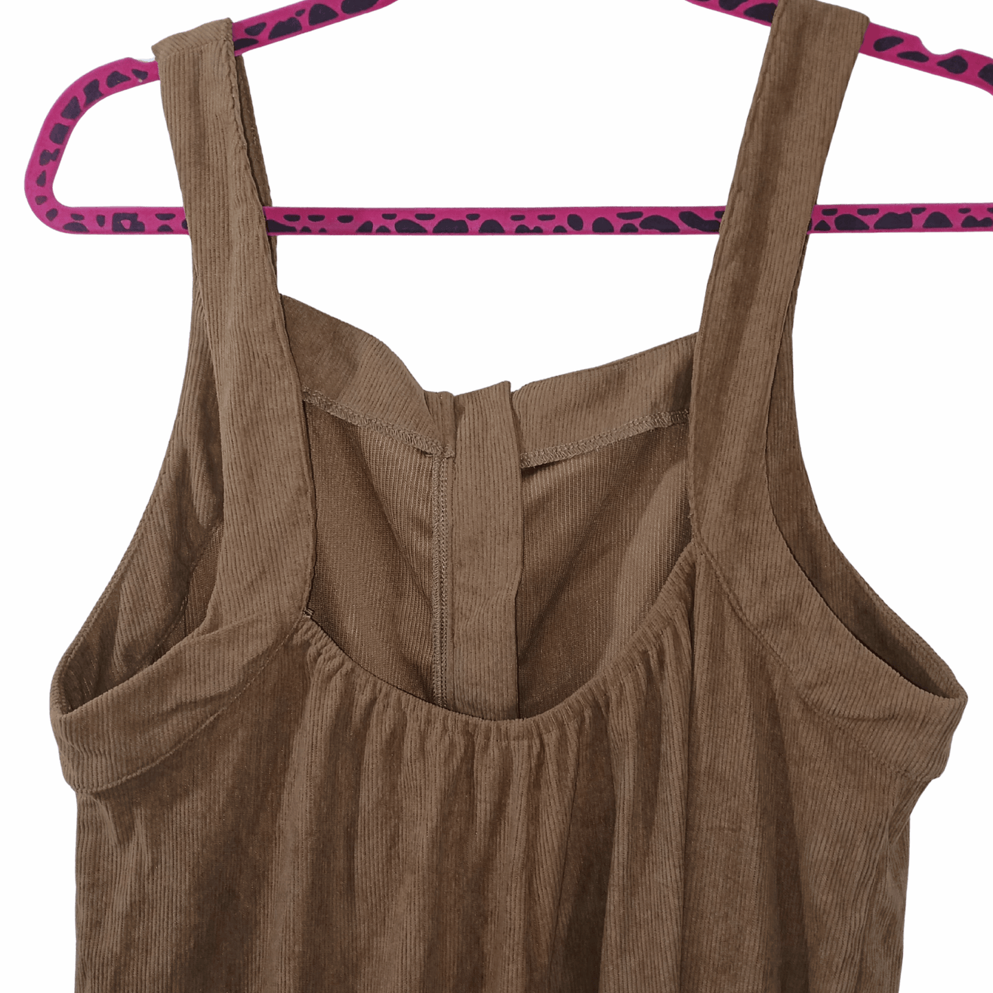 Brown corduroy pinafore dress on a pink hanger against a gray background