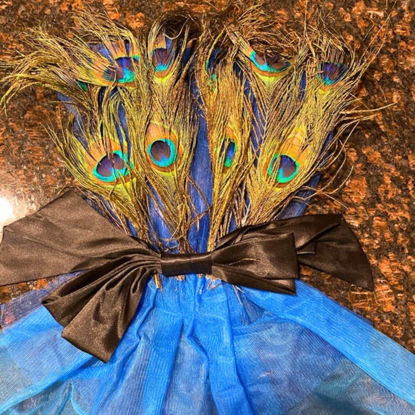 Blue dress with peacock feathers and a black bow on a textured surface