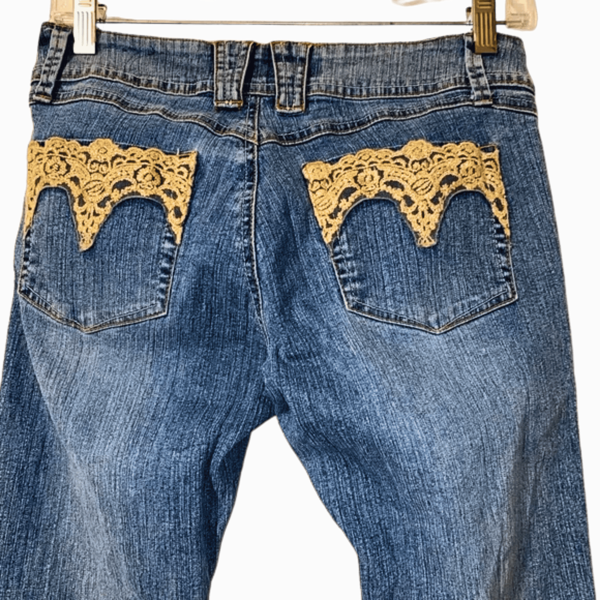 Blue jeans with gold lace detailing on the pockets against a gray background