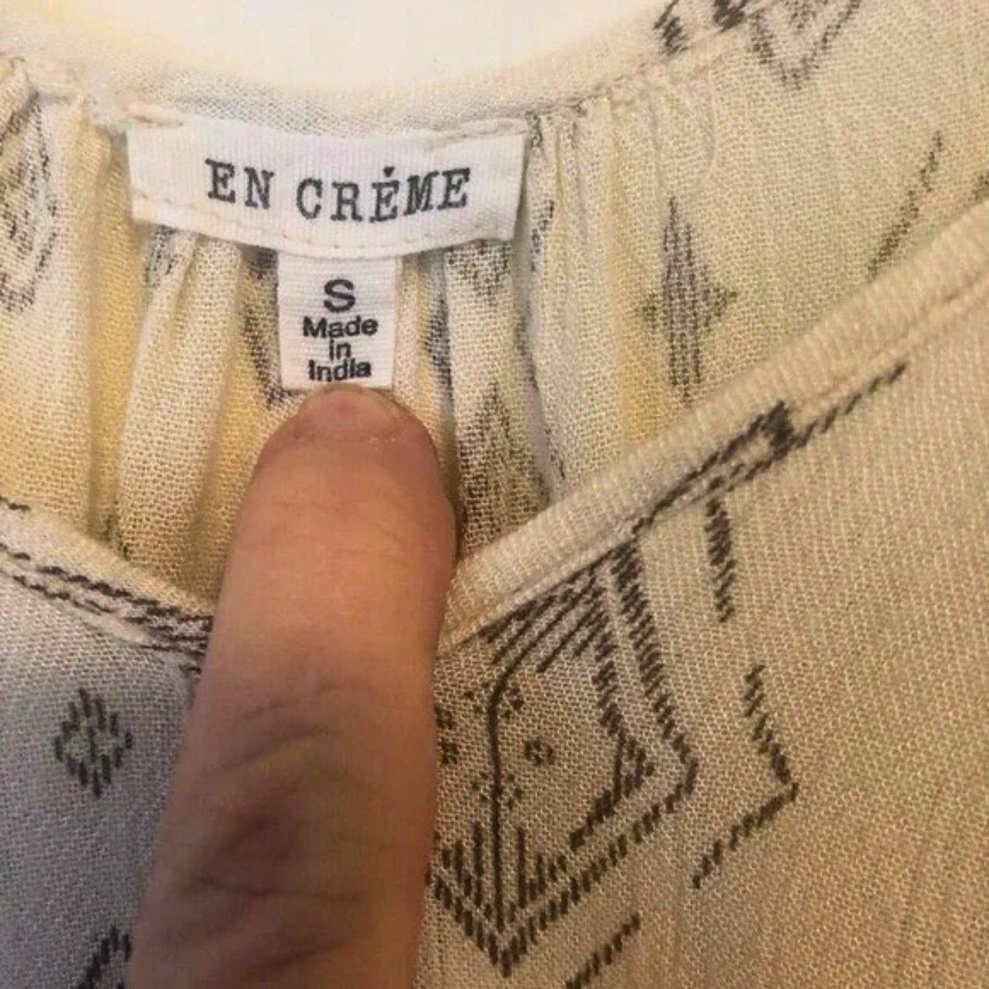 Fabric with 'EN CREME' label and size tag, finger pointing at the label.