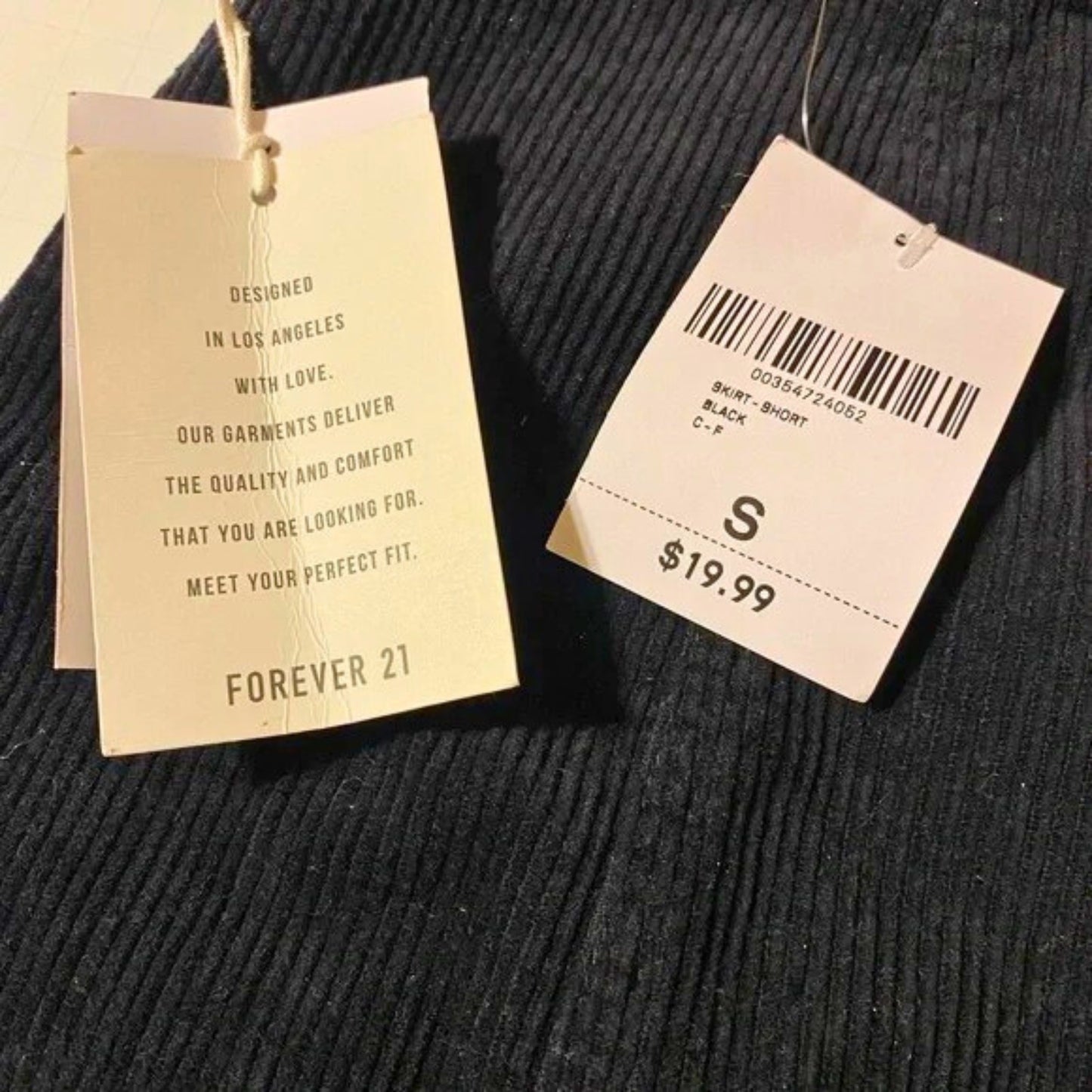 Two tags on a black textured fabric background, one with text and the other with a barcode and price.