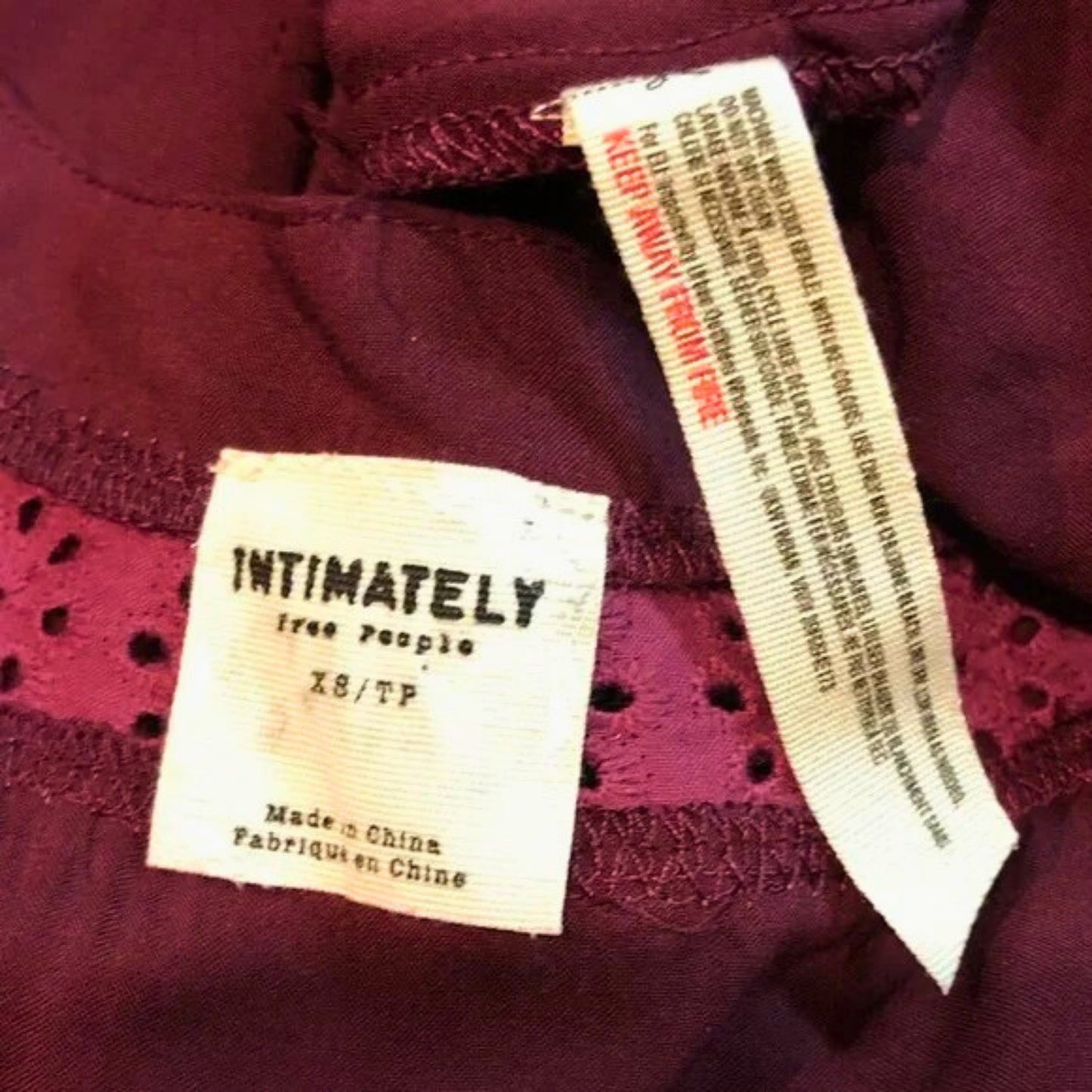 Close-up of a clothing label on a maroon garment with text.