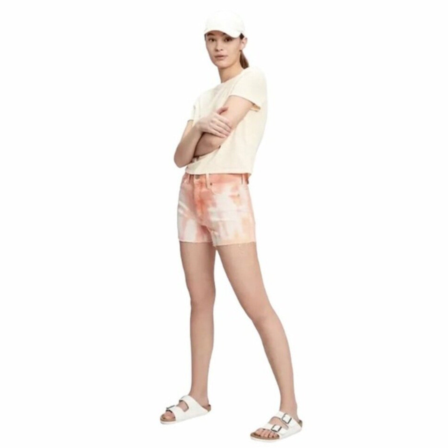 Woman wearing a light-colored t-shirt and tie-dye shorts on a white background