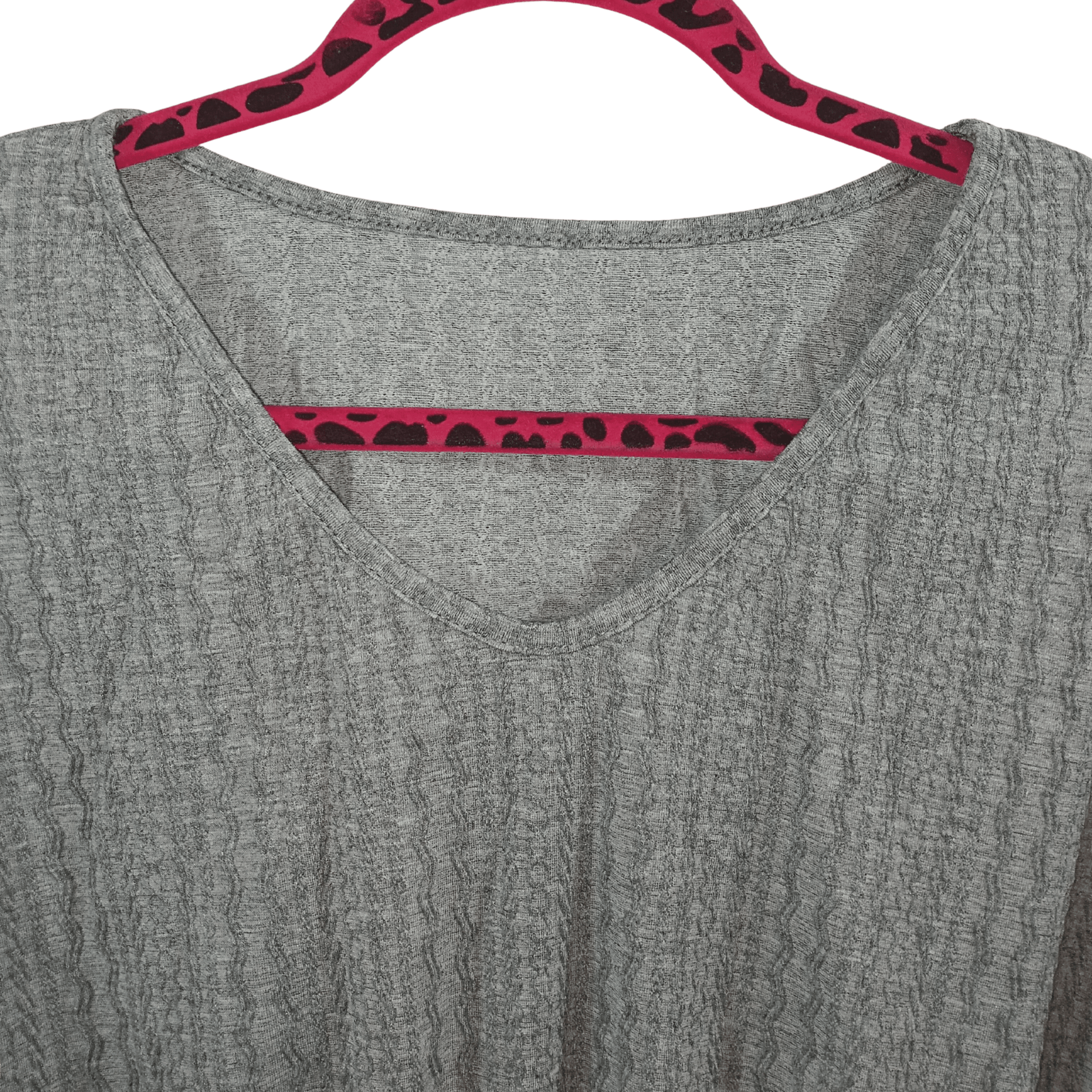 Gray shirt with red and black patterned trim on a hanger against a green background