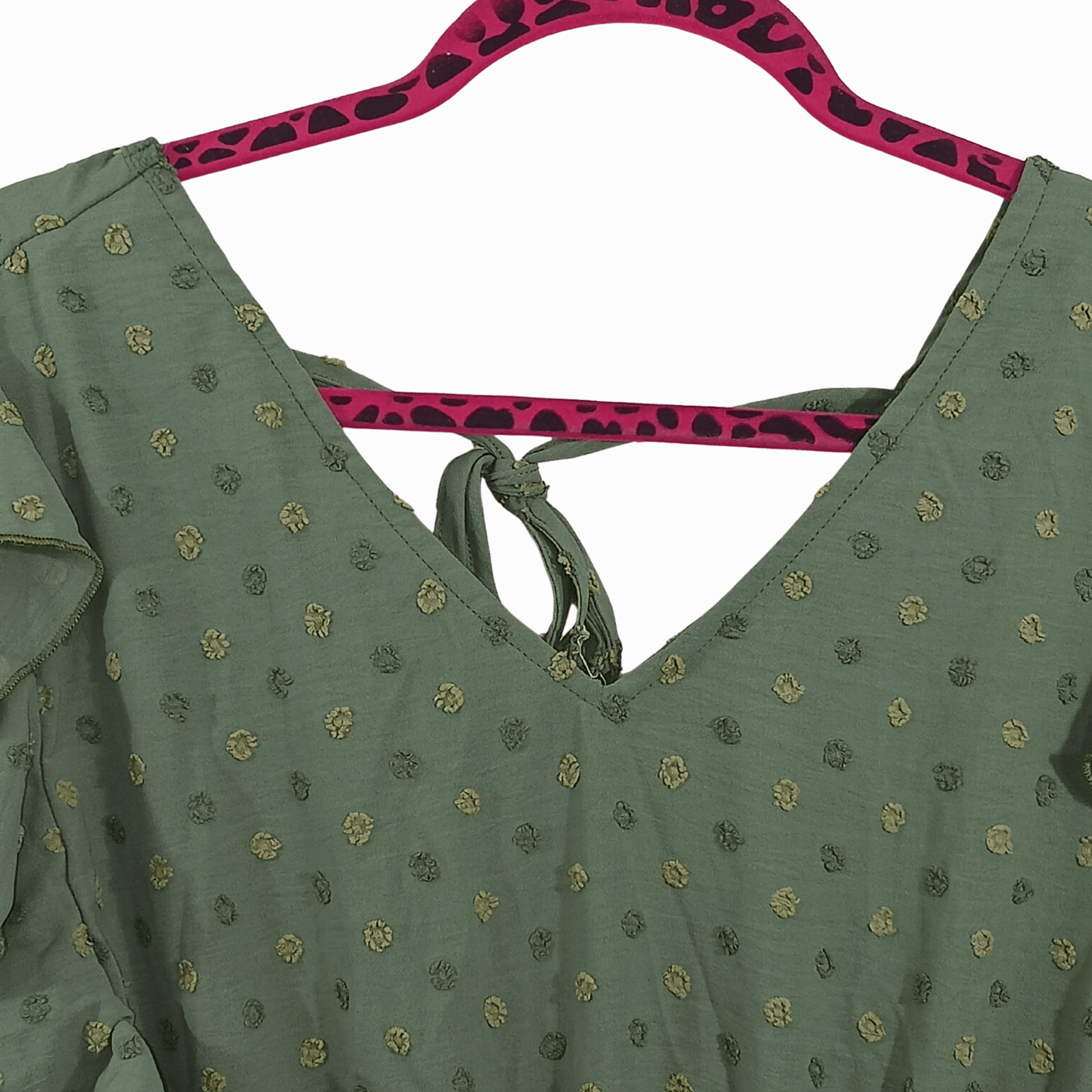 Green blouse with gold patterns on a pink hanger against a dark background