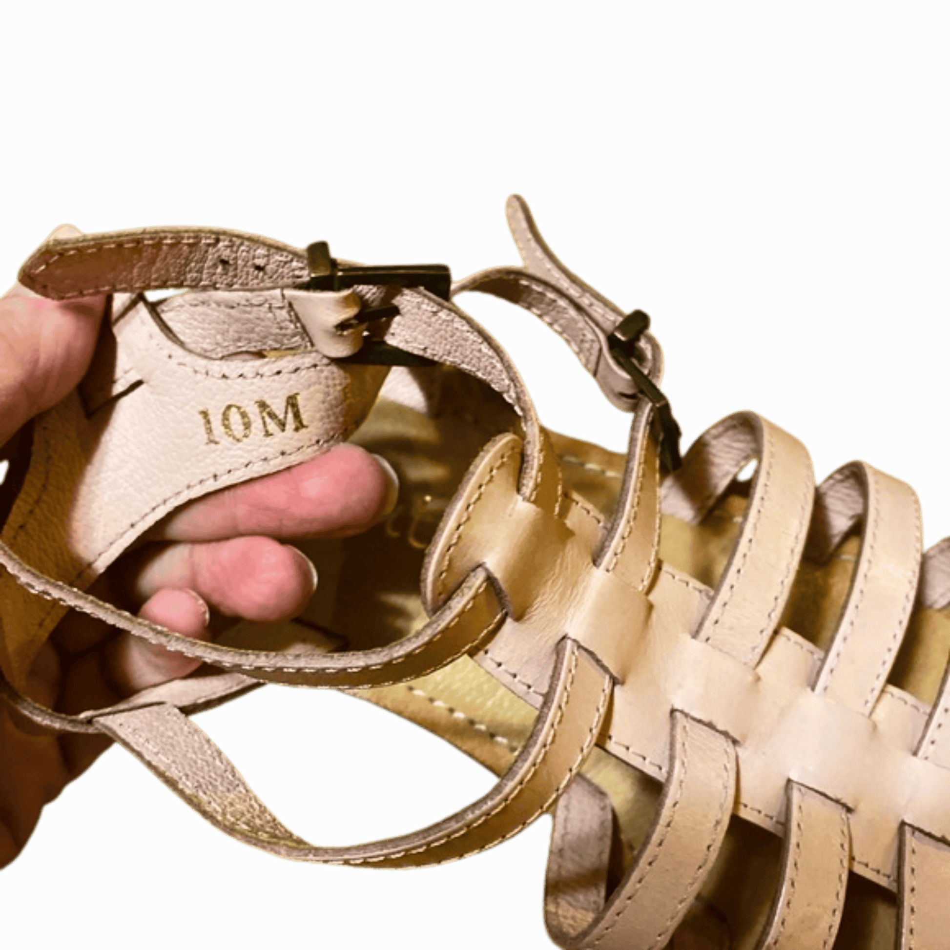Beige sandal with '10M' marking held by a hand against a red background