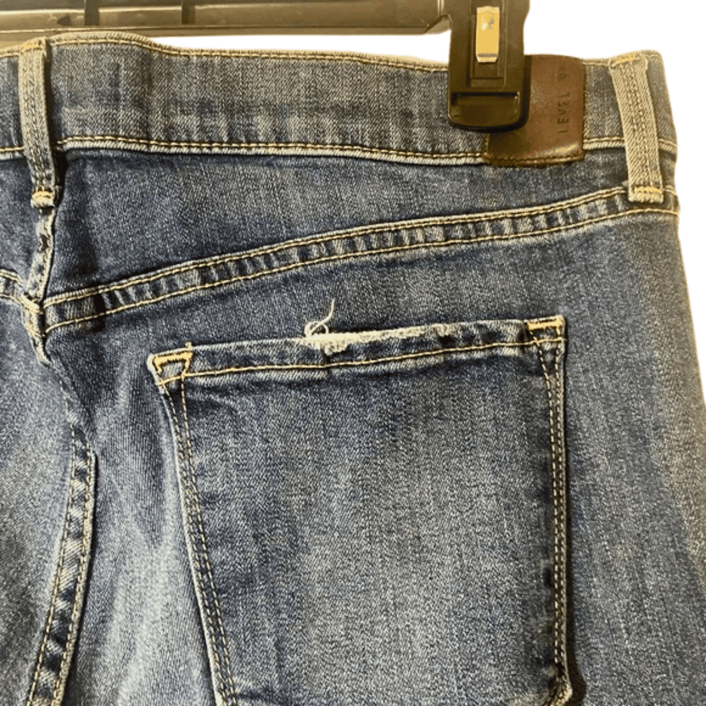 Close-up of a blue denim jeans back pocket on a hanger with a green background