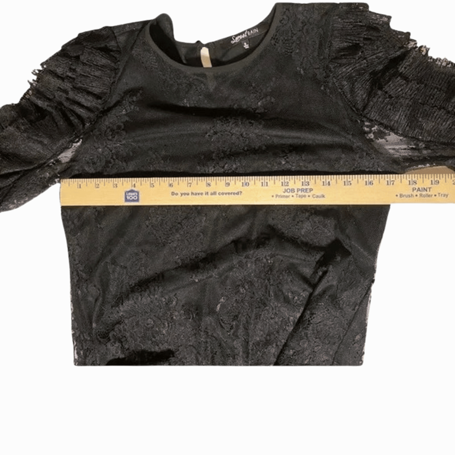 Black textured long-sleeve top with a ruler for size reference on a gray background