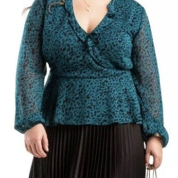 Woman wearing a teal patterned top and black pleated skirt holding a beige handbag on a white background