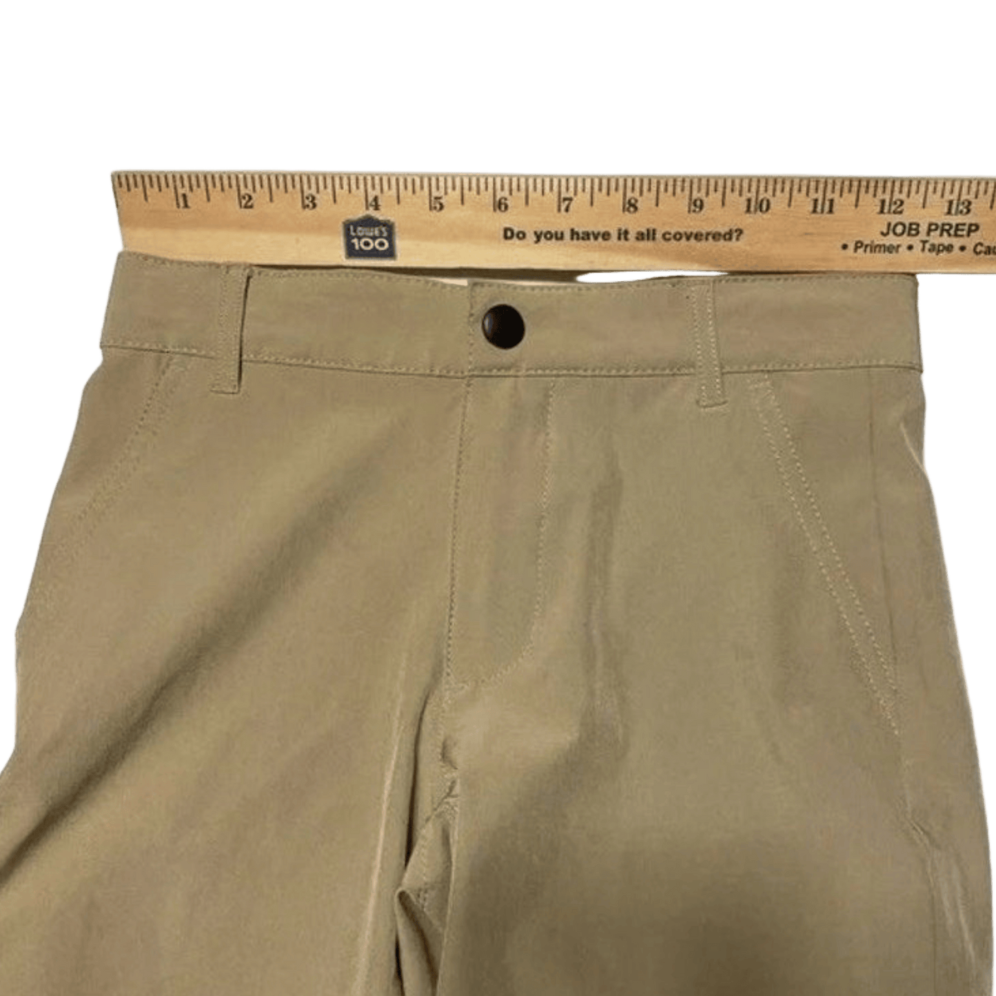 Beige pants with a ruler on top against a green background