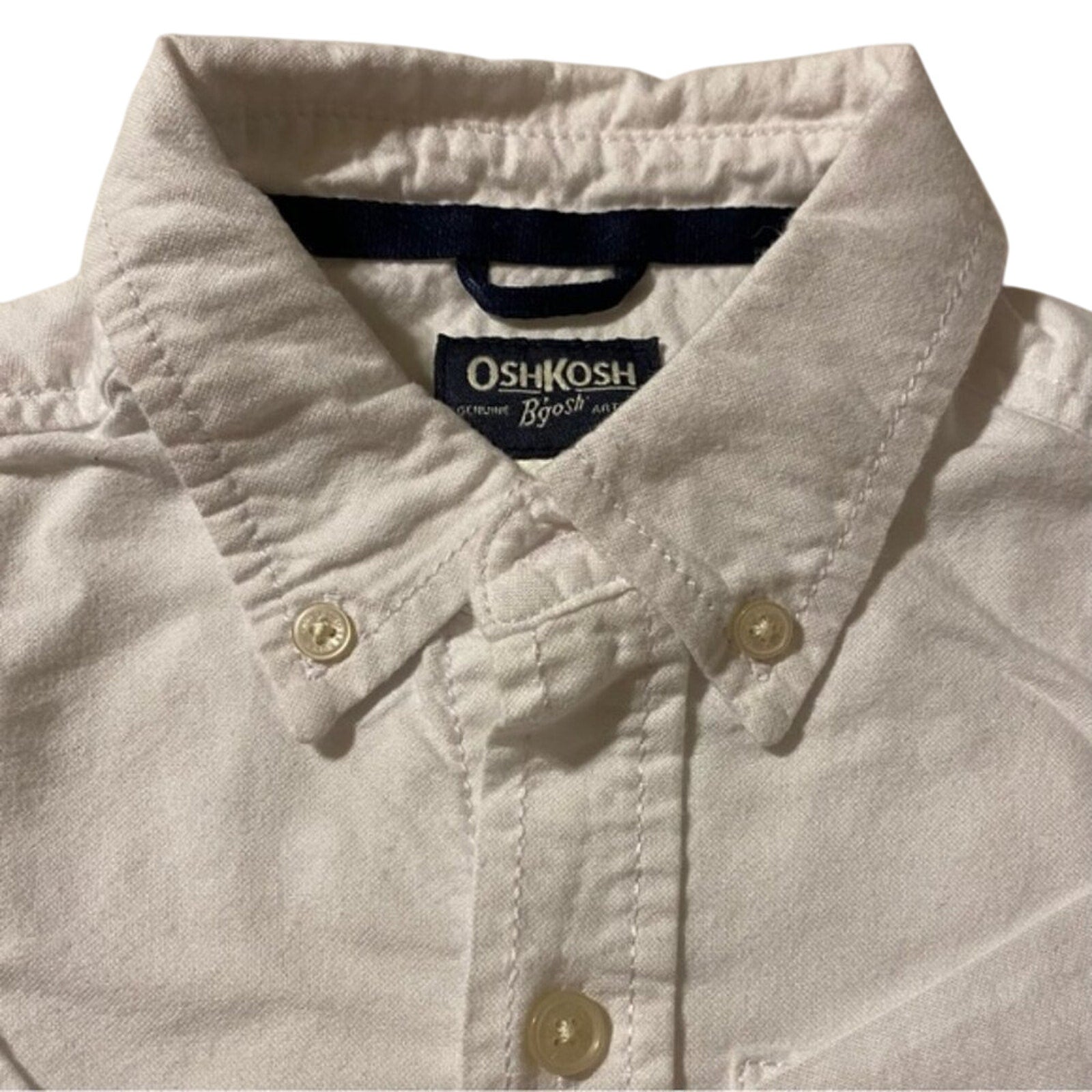 Close-up of a light-colored shirt with OshKosh logo on a white background