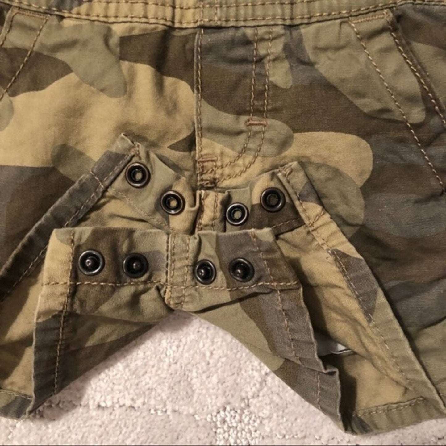 Close-up of a camouflage jacket with button details on a textured surface