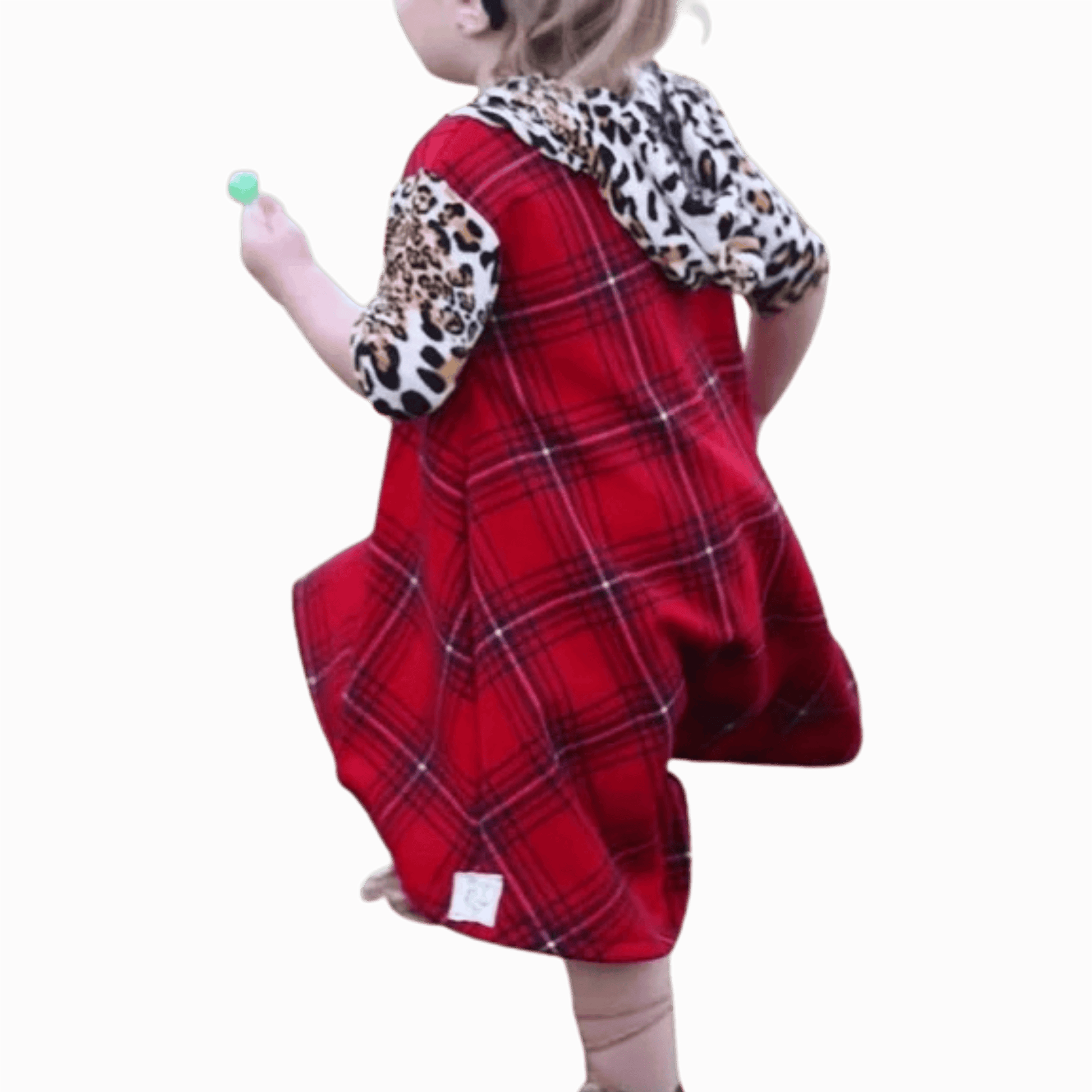 Child wearing a red plaid dress with leopard print sleeves on a brown background