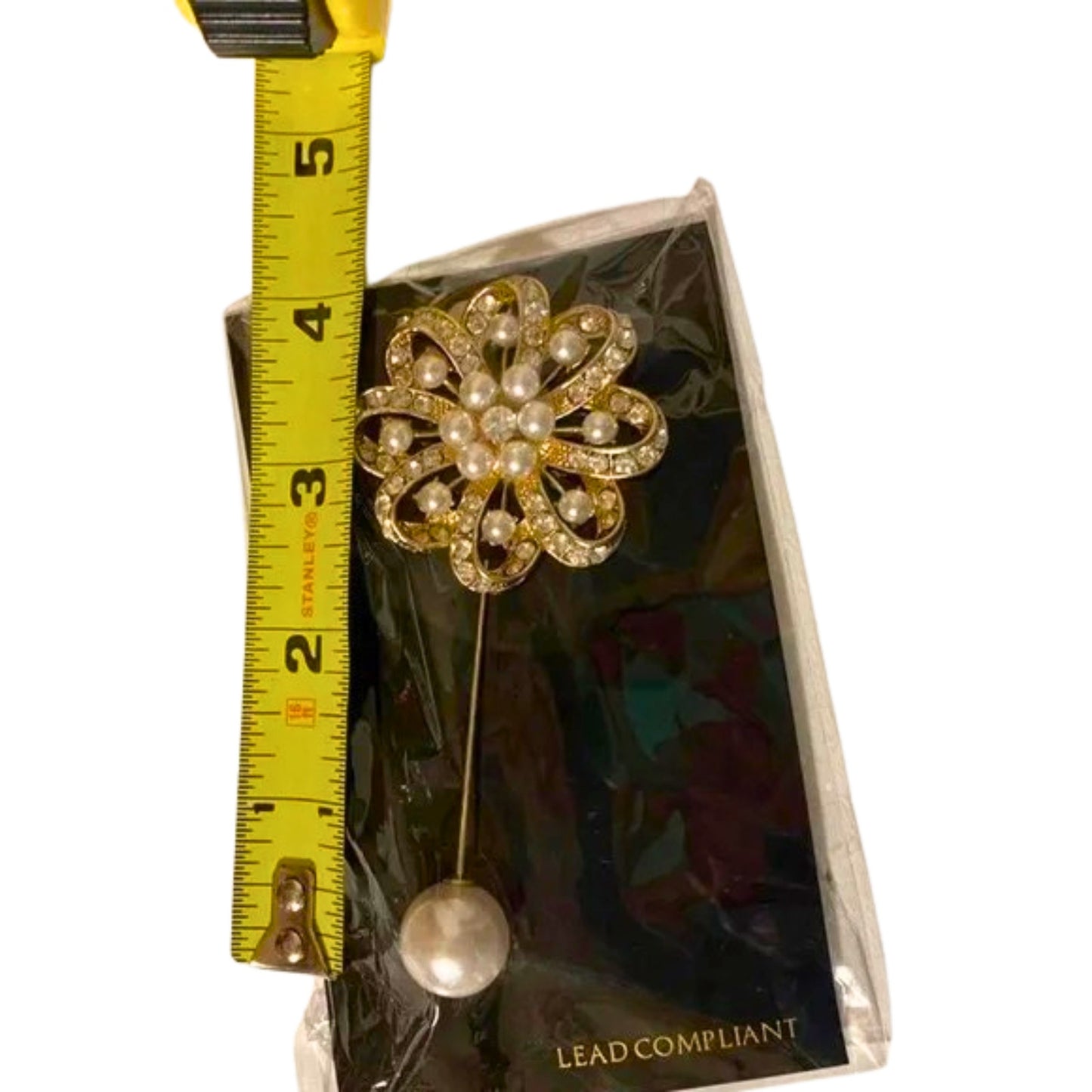Floral brooch with pearls on a card, measured against a tape measure