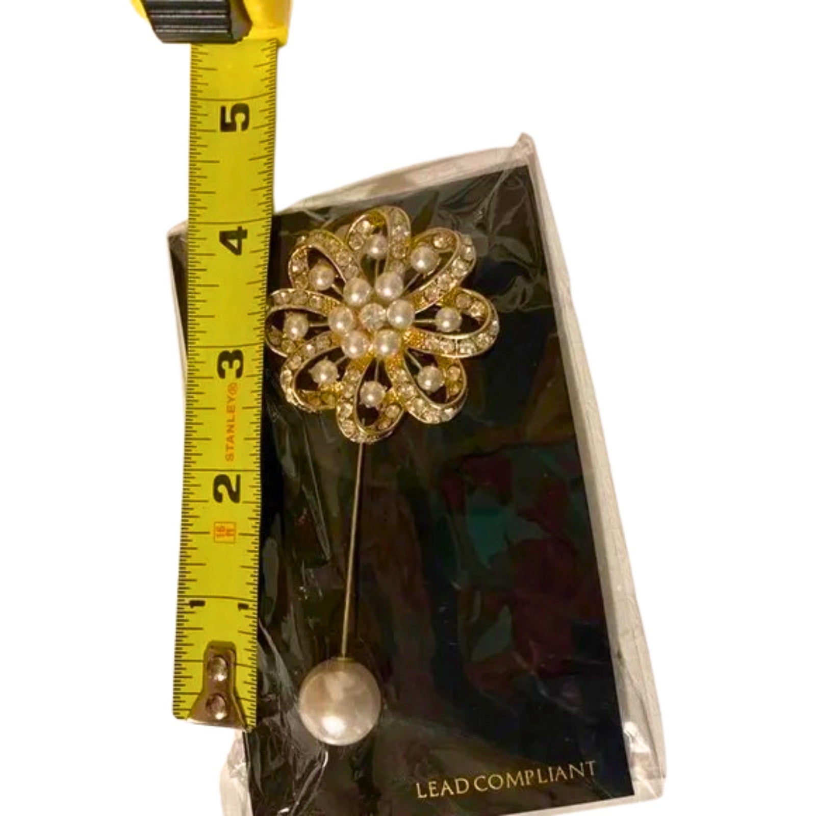 Floral brooch with pearls on a card, measured against a tape measure