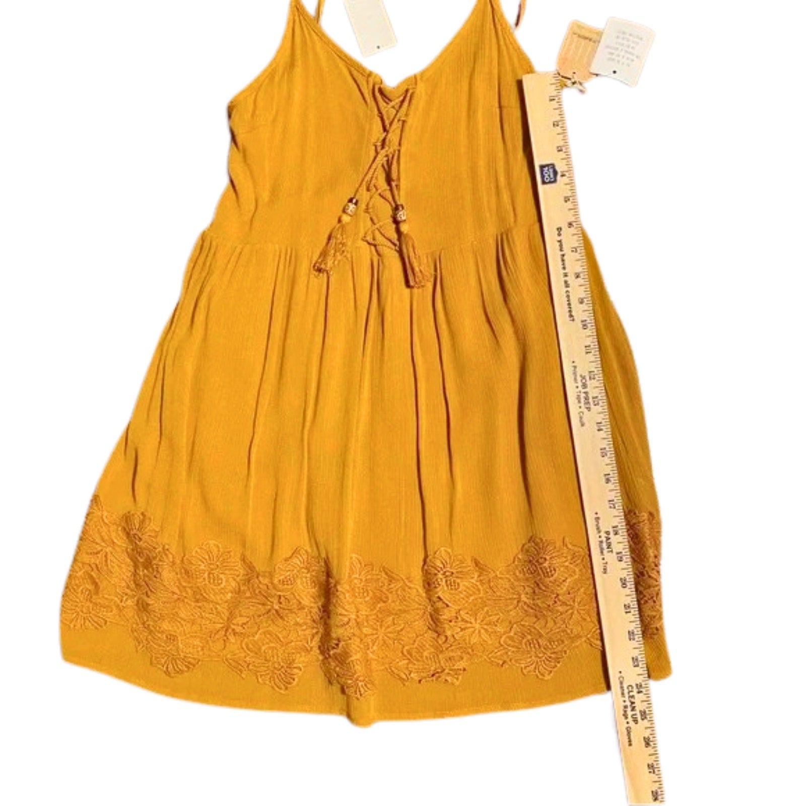 Mustard yellow dress with floral embroidery and a measuring tape on a white background