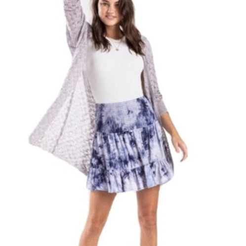 Woman wearing a white top, gray cardigan, and tie-dye skirt on a white background