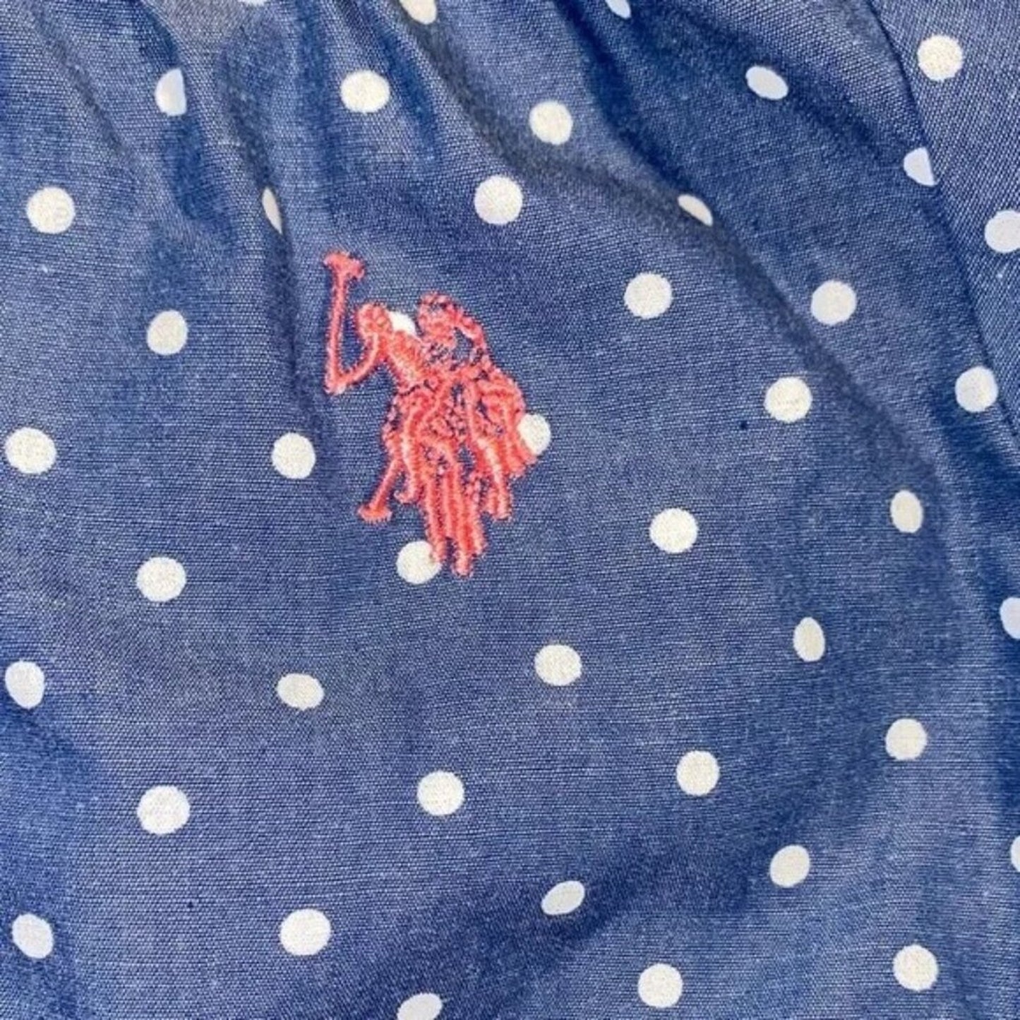 Close-up of a blue fabric with white polka dots and a red logo.