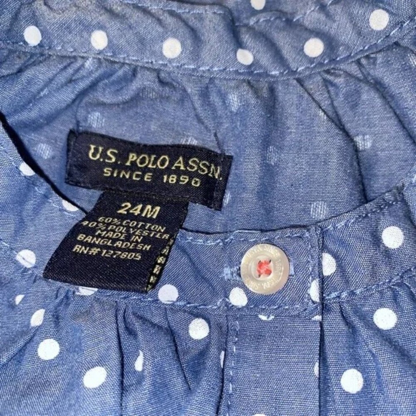 Close-up of U.S. Polo Assn. label on a blue polka dot shirt with a button.