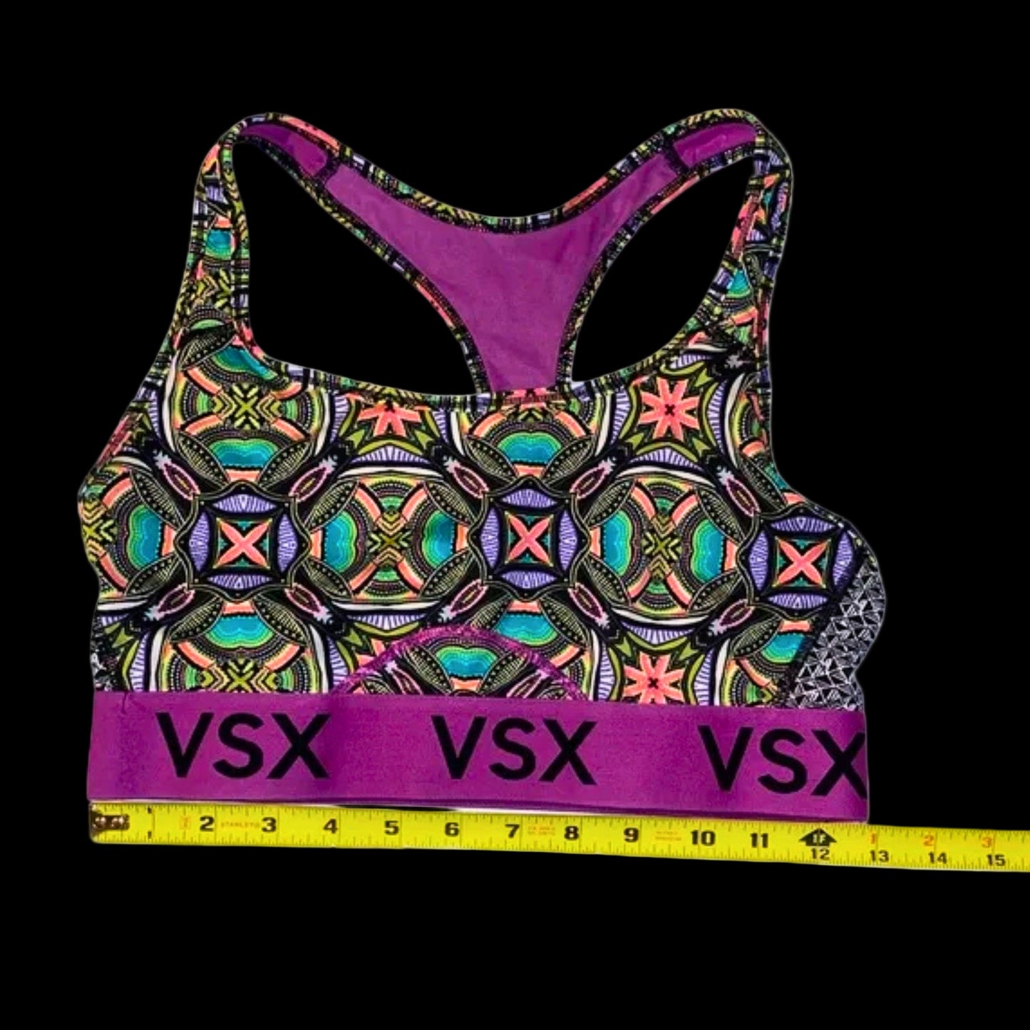 Colorful patterned sports bra with 'VSX' branding, measured against a tape measure on a white background.