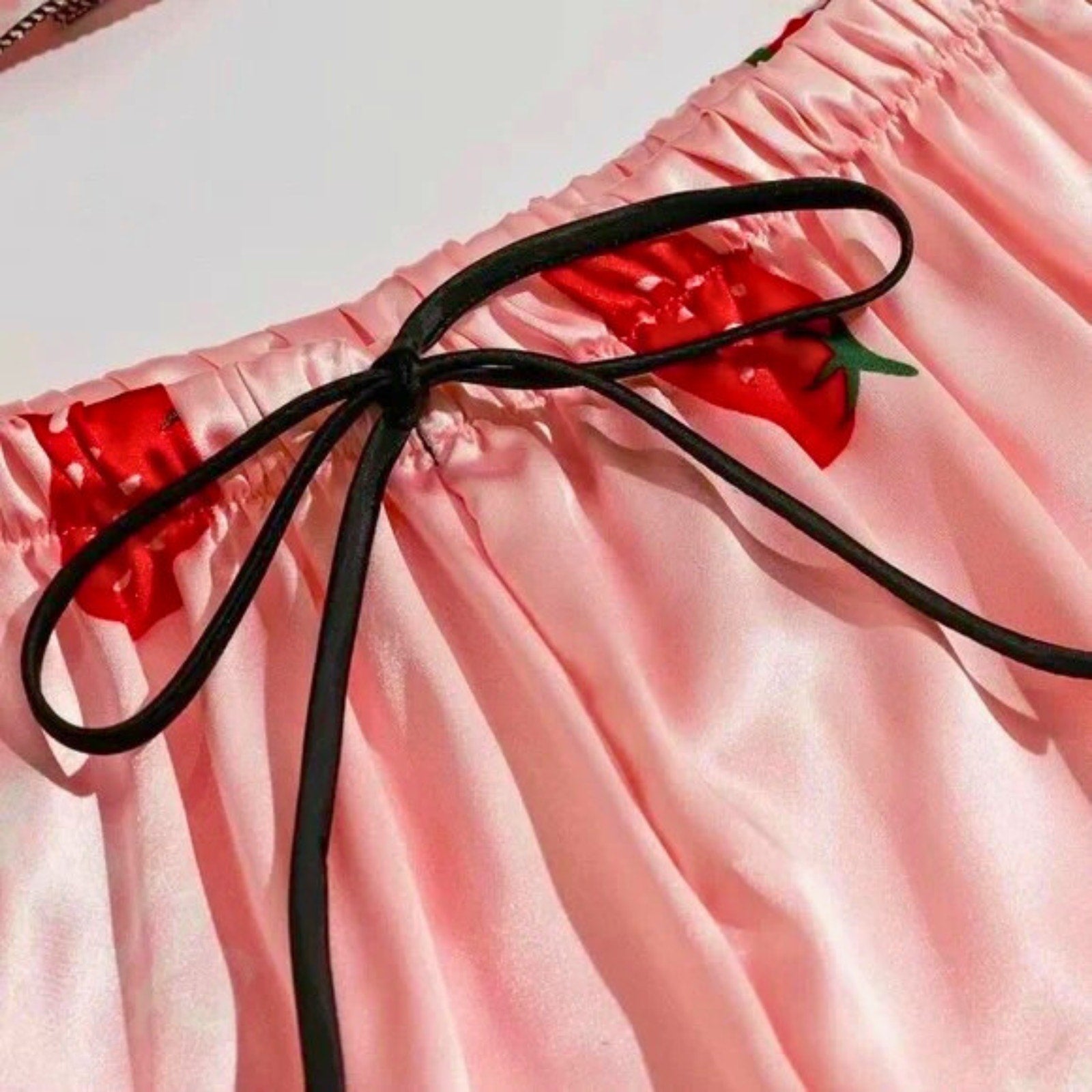 Close-up of pink shorts with red strawberry design and black drawstring.
