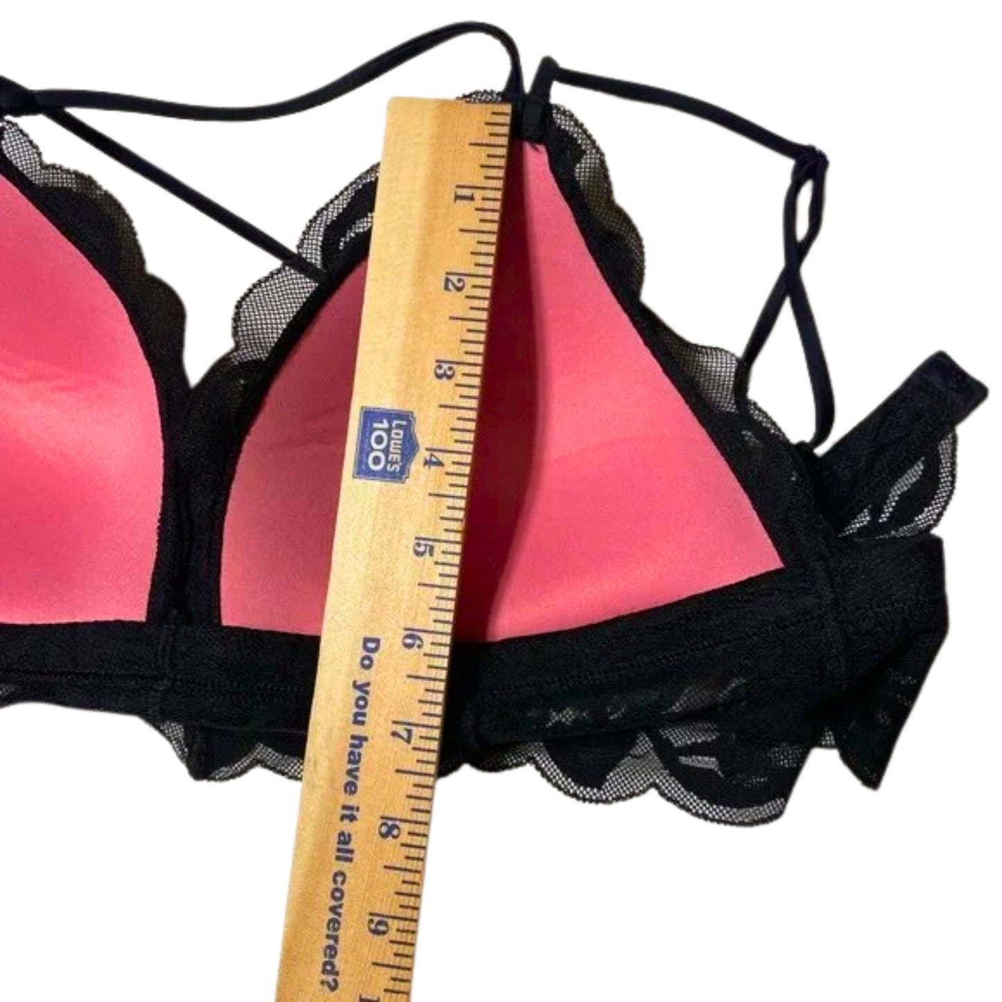 Pink bra with black lace trim and a ruler for size reference on a white background