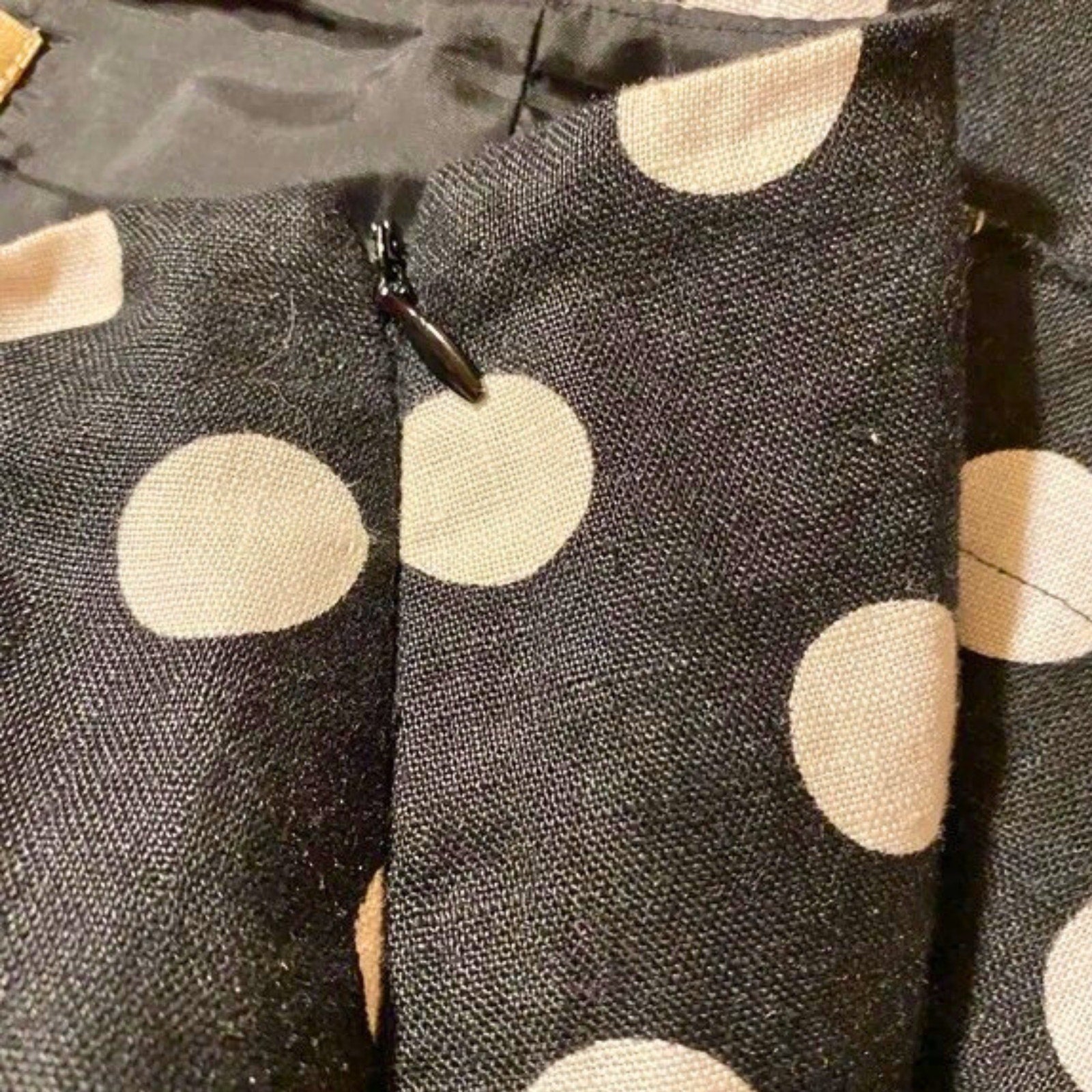 Close-up of a black fabric with beige polka dots and a zipper.