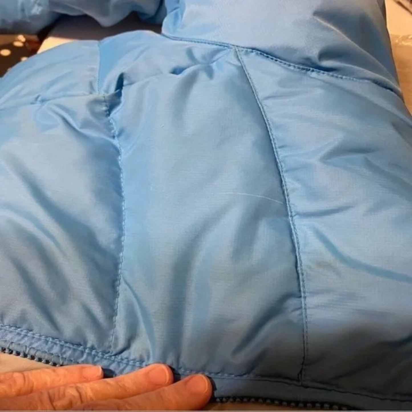 Close-up of a blue puffer jacket with a hand holding the bottom hem.