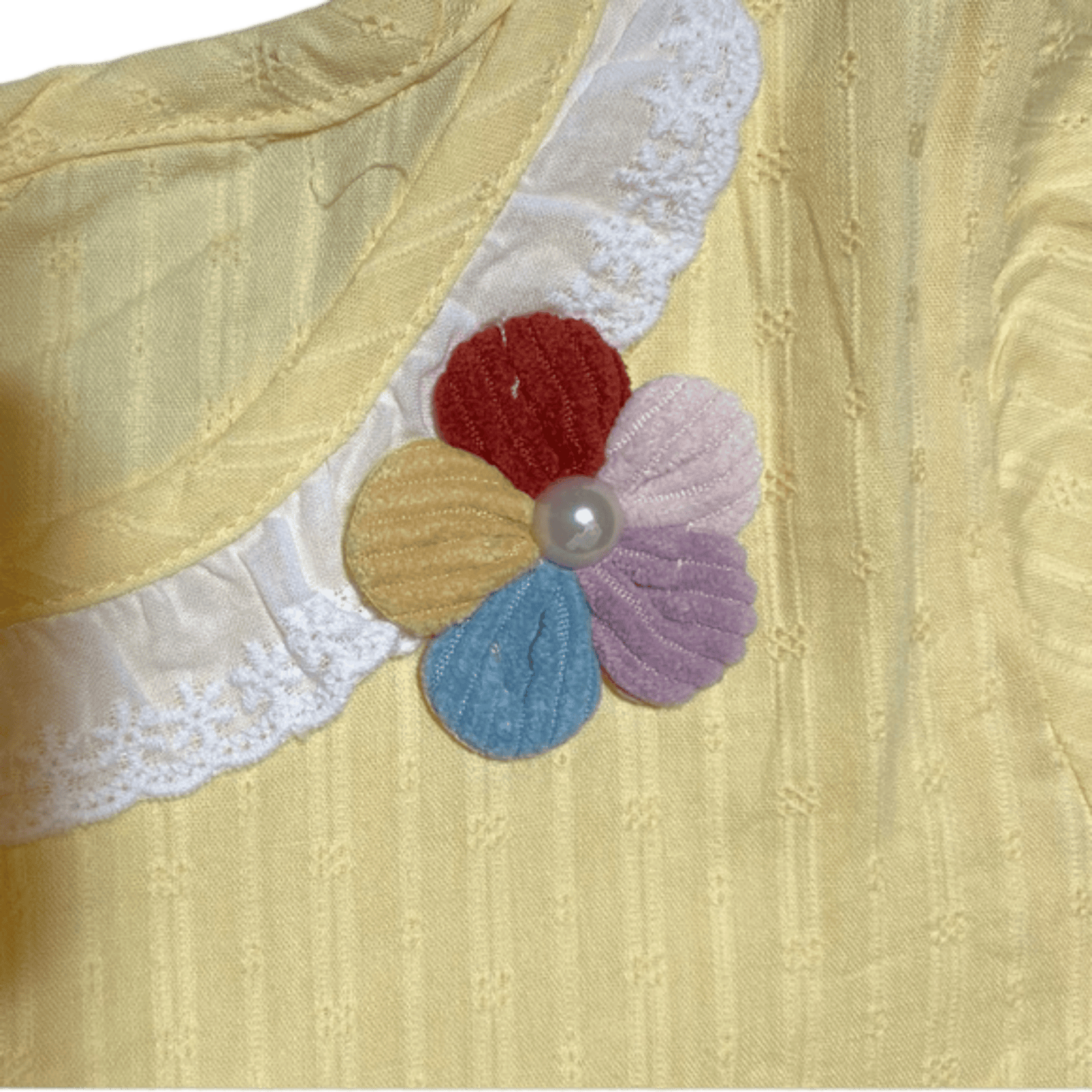 Close-up of a yellow fabric with a colorful flower appliqué and lace trim.
